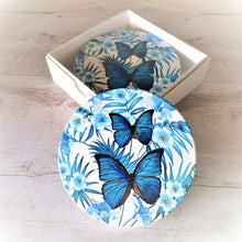 Load image into Gallery viewer, Introduce elegance with our Butterfly Blue Coaster Gift Set. Made of round ceramic coasters, these four pieces feature a butterfly design that adds beauty to your kitchen table. Perfectly boxed, this set makes an impressive gift for any occasion.  Beautiful gift for the bar, coffee table, patio or kitchen.  Round ceramic coasters | Set of 4 | Glossy finish | White gift box | Cork non slip backing | Diameter 10 cm | Set of 4 same design.