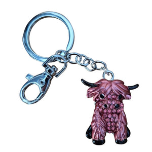 Crafted from silver metal, this hand-painted keychain features a pink and black Highlander cow adorned with pink rhinestones. Measuring 11.5 cm in total length, the cow itself is 3.5 x 4 cm. Each bag chain keyring is presented in a cotton organza pouch, with colors that may vary.
