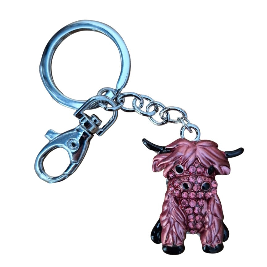 Crafted from silver metal, this hand-painted keychain features a pink and black Highlander cow adorned with pink rhinestones. Measuring 11.5 cm in total length, the cow itself is 3.5 x 4 cm. Each bag chain keyring is presented in a cotton organza pouch, with colors that may vary.