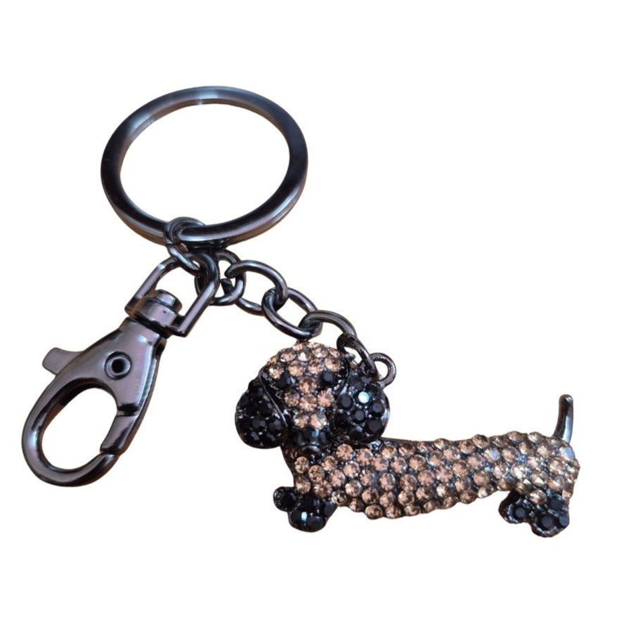  This charming small dachshund sausage dog keyring measures 10 cm in total length, with the dog itself sized at 4.5 x 2.2 cm. Crafted with black gun black metal and detailed with brown and black rhinestones, it makes a perfect gift for sausage dog enthusiasts.