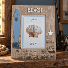 Load image into Gallery viewer, A rustic wooden picture frame with a nautical beach theme, featuring a blue fish silhouette, a white star, a seashell photo insert, and the word 'BEACH' at the top, displayed on a wooden surface with fishing rods and rope in the background.