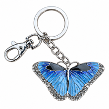 Load image into Gallery viewer, A butterfly-shaped keychain charm with vibrant blue and black wings, bordered with small clear rhinestones, attached to a silver-tone chain and key ring on a plain white background.