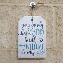 Load image into Gallery viewer, This ceramic hanging sign is the perfect family home gift. Display the heartwarming message &quot;Every Family Has A Story To Tell, Welcome To Ours&quot; in any room of your home. Celebrate the unique story of your family with this charming and sentimental piece.