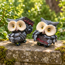 Load image into Gallery viewer, Two owl garden statues with large cream-colored eyes and dark gray bodies, each holding a small sign that reads 'Welcome', placed on a mossy stone ledge with a blurred green garden background.