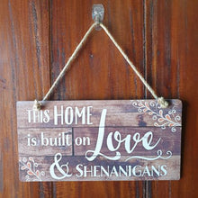 Load image into Gallery viewer, Add a touch of humor to your home with our &quot;This Home Is Built On Shenanigans&quot; hanging sign. Crafted with quality materials, this sign is the perfect addition to your home decor. Let everyone know your house is filled with laughter and good times.