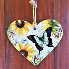 Load image into Gallery viewer, Our beautiful sunflower and butterfly design is the perfect bright uplifting gift to brighten up someone&#39;s day.  Heart shaped | 16 x 19 cm + rope hanger | Ceramic | Cork backing | Gloss finish.  Design is also available in serving table tray, cheeseboard &amp; square bench kitchen trivet.